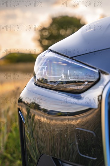 Close-up of a car headlight in the evening, reflecting the surroundings of a field, BMW i7 electric car, deer e-car sharing, Calw, Germany