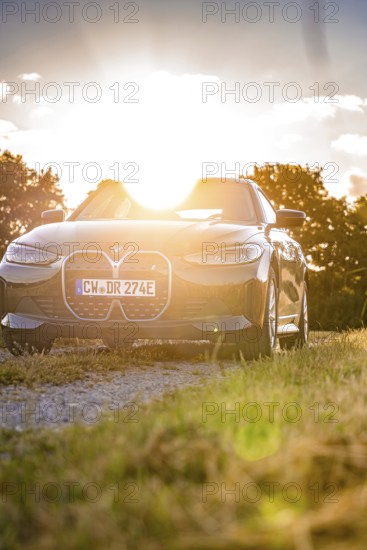 Black electric car on a dirt road in the backlight of the setting sun, atmospheric light-flooded scene, BMW i7 electric car, deer e-car sharing, Calw, Germany
