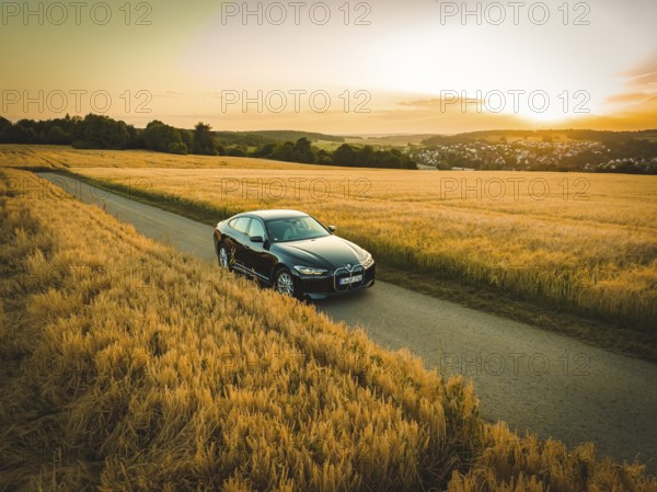 Car driving on a dirt road through golden fields at sunset with rural views, BMW i7 electric car, deer e-car sharing, Calw, Germany
