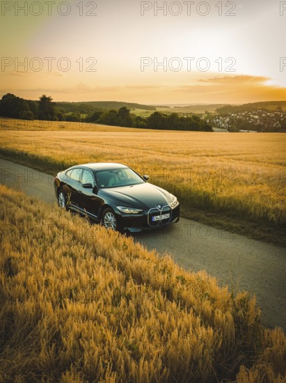 Black car on a country road between wheat fields at sunset, BMW i7 electric car, deer e-car sharing, Calw, Germany