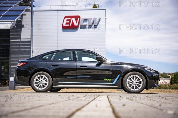 Black car in front of a building with a large company logo under blue sky, BMW i7 electric car, Deer e-Carsharing, Calw, Germany