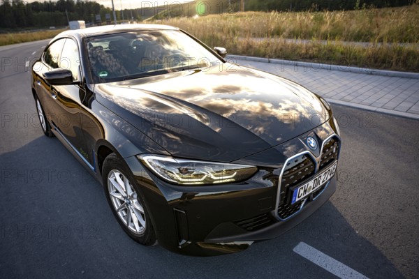 A black car on a road with reflecting sky and a field, BMW i7 electric car, Deer e-Carsharing, Calw, Germany