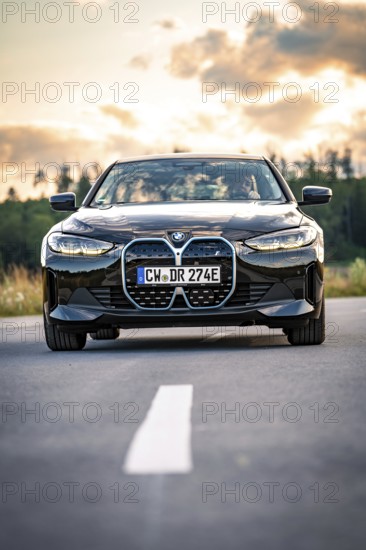 A black car on a country road at sunset with trees in the background, BMW i7 electric car, Deer e-Carsharing, Calw, Germany