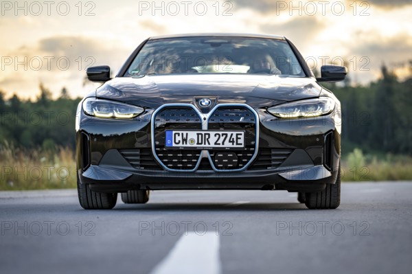Front view of a black car on the road in front of a forest at sunset, BMW i7 electric car, Deer e-Carsharing, Calw, Germany
