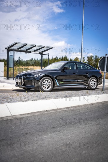 Black car at a modern bus stop under blue sky, BMW i7 electric car, Deer e-Carsharing, Calw, Germany