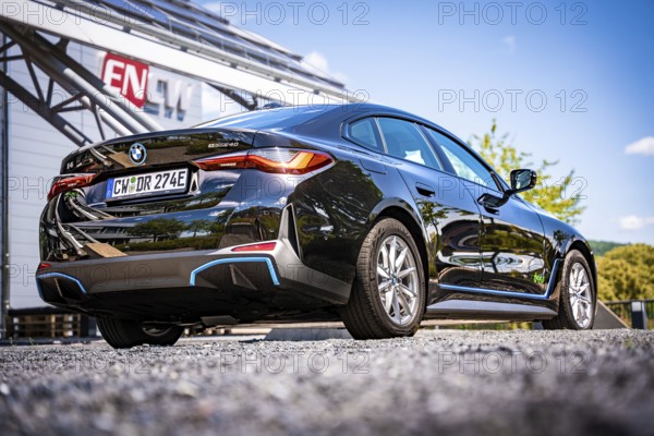 Rear view of a black car in front of a modern building with ENCW logo and blue sky, BMW i7 electric car, Deer e-Carsharing, Calw, Germany