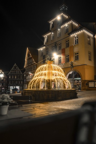 Overview of illuminated fountains in front of traditional buildings in a nocturnal town, Calw, Black Forest, Germany