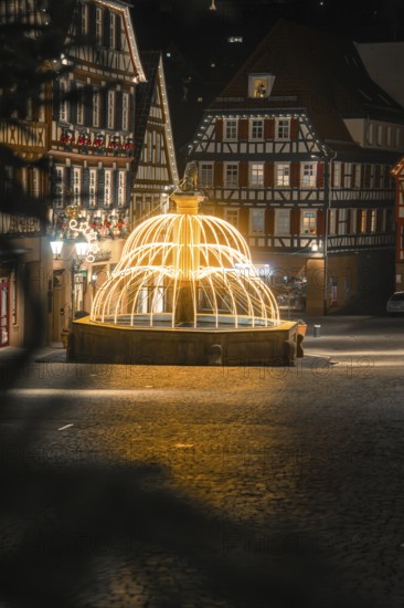 Nocturnal scene with illuminated fountain surrounded by traditional half-timbered houses, Calw, Black Forest, Germany