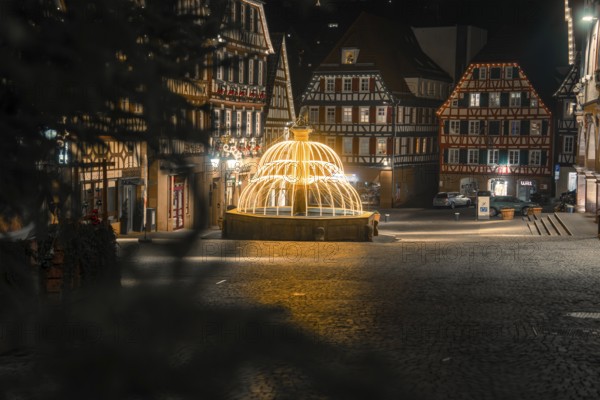 Idyllic night scene with illuminated fountain and traditional buildings in the city center, Calw, Black Forest, Germany
