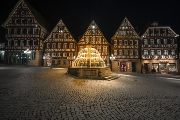 Illuminated fountain in a historic city center with half-timbered buildings at night, Calw, Black Forest, Germany