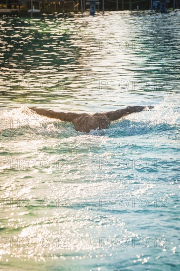 A swimmer in the pool with arms spread out, the water surface shimmers in the light, triathlon, Calw, Germany