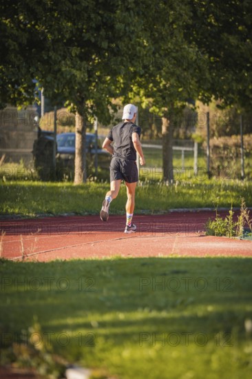 A jogger runs on a red track in the countryside, surrounded by trees on a sunny day, triathlon, Calw, Germany