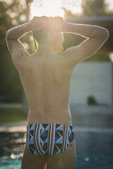 A man in swimming trunks stands by the pool in sunlight and enjoys the relaxed atmosphere, Triathlon, Calw, Germany