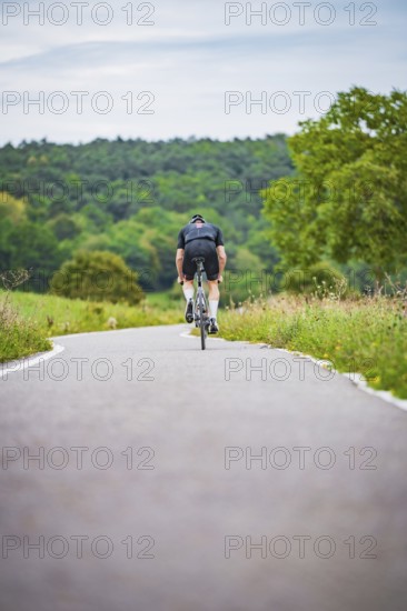 A cyclist rides on a remote road through nature, with trees and grass, triathlon, Calw, Germany
