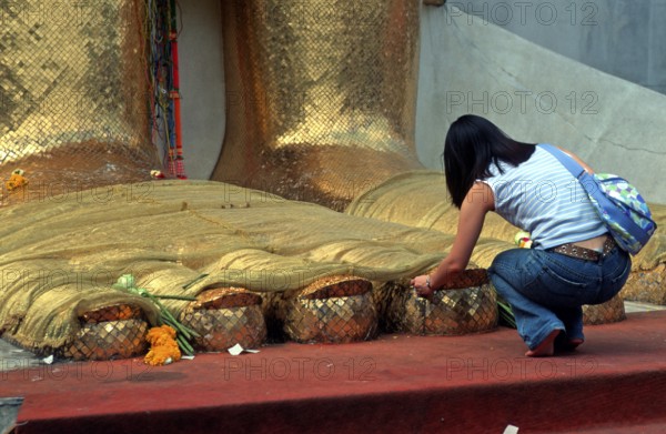 A young woman places flowers on the toes of the standing Buddha at Wat Indrawihan, Bangkok, Thailand, December 2002, vintage, retro, old, historic