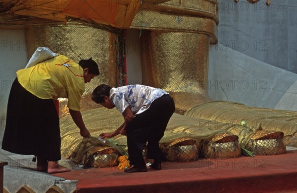 Women place flowers on standing Buddha's toes at Wat Indrawihan, Bangkok, Thailand, December 2002, vintage, retro, old, historic
