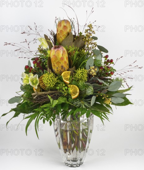 Exotic flower arrangement with protea, Christmas rose and berries in a glass vase, presented decoratively