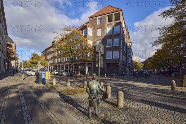 Bronze sculpture newspaper boy, sculptor Frauke Wehberg, street made of paving stones, general architecture, houses, residential buildings and commercial buildings, barrier bollard, pedestrian zone, parking strips with cars, trees, autumn leaves, blue sky, cumulus clouds, intersection of Fleethörn, Willestraße and Asmus-Bremer-Platz, Kiel, state capital, district-free city, Schleswig-Holstein, Germany