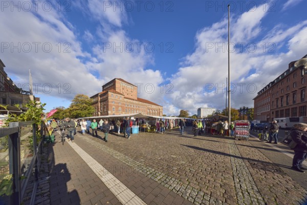 Opera house, general architecture, historic brick building, brick architecture, square, flagpoles, market stalls, market visitors and pedestrians as accessories, sidewalk made of concrete paving stones, cobblestones and paving stones, blue sky, cumulus clouds, town hall square, Kiel, state capital, district-free city, Schleswig-Holstein, Germany