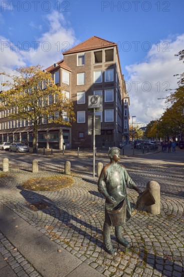 Bronze sculpture newspaper boy, sculptor Frauke Wehberg, street made of paving stones, general architecture, houses, residential buildings and commercial buildings, barrier bollard, pedestrian zone, parking strips with cars, trees, autumn leaves, blue sky, cumulus clouds, intersection of Fleethörn, Willestraße and Asmus-Bremer-Platz, Kiel, state capital, district-free city, Schleswig-Holstein, Germany