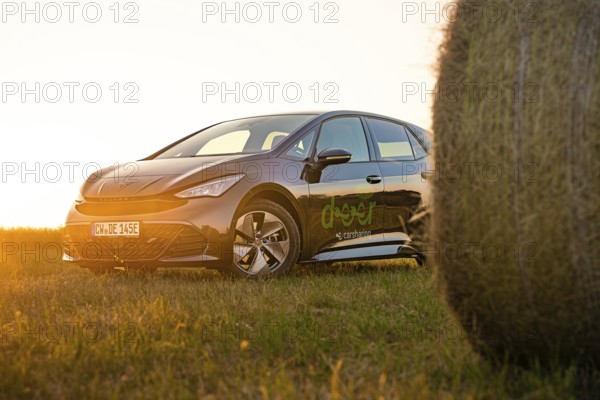 Car next to a hay bale in a rural landscape at sunset, electric car Cupra, e-car sharing, Calw, Germany