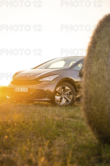 Car in the golden light of sunset in a meadow next to a hay bale, electric car Cupra, e-car sharing, Calw, Germany