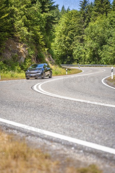 Black car on winding country road along green forests in sunny ambiance, Cupra electric car, e-car sharing, Calw, Germany
