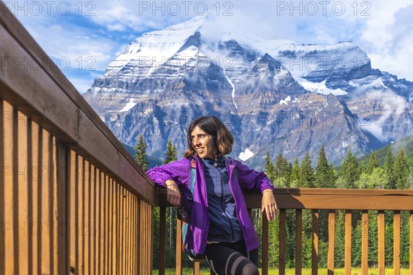 Female hiker is taking a break and enjoying breathtaking view of mount robson, the highest peak in the canadian rockies, british columbia, canada, during a sunny summer day