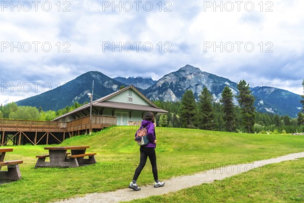 Female tourist walking on a path in mount robson provincial park with visitor center and picnic area and mount robson in the background, canadian rockies, british columbia, canada