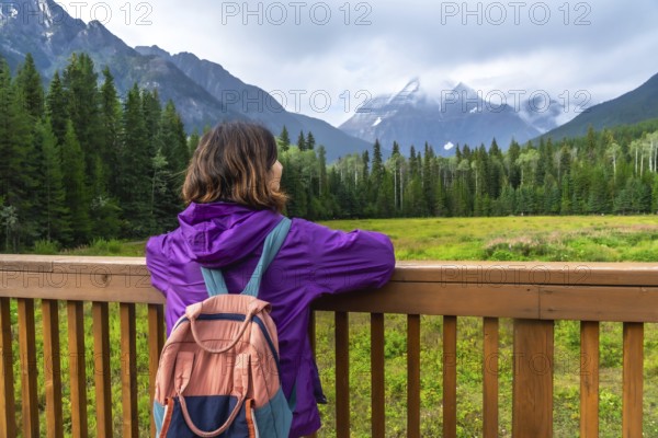 Female hiker with backpack enjoying the scenic view of mount robson, the highest peak in the canadian rockies, british columbia, canada, during a cloudy day