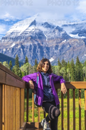 Female hiker is taking a break on a wooden platform, enjoying the breathtaking view of mount robson, the highest peak in the canadian rockies, british columbia, canada