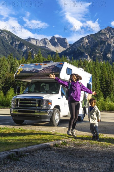 Happy mother and son are jumping in front of their recreational vehicle near mount robson in the canadian rockies, british columbia, canada, enjoying their summer vacation