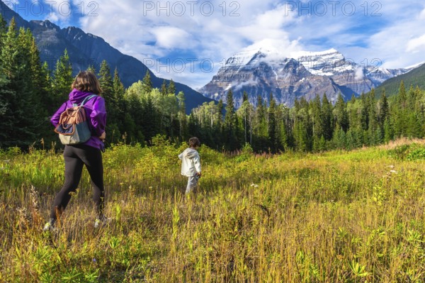 Hikers traversing a vibrant meadow under the warm sun, with mount robson towering majestically in the background, create a stunning scene in the canadian rockies of british columbia