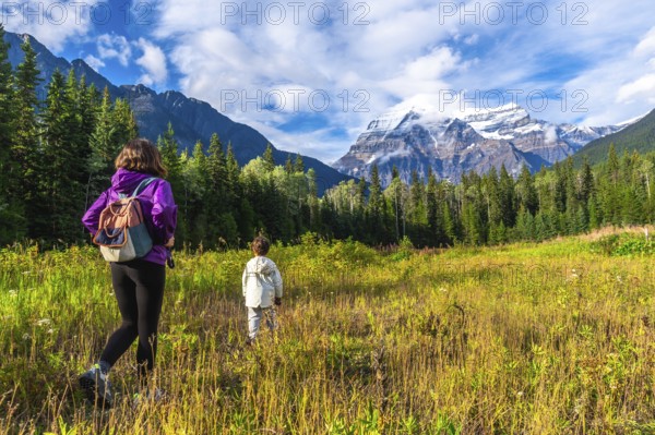 Hikers are enjoying a scenic walk through a meadow with majestic mount robson towering in the distance, showcasing the natural beauty of the canadian rockies in british columbia, canada