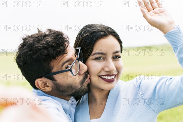 Selfie of young happy couple kissing in the field. Cute couple in love taking a selfie in the field, looking at the camera