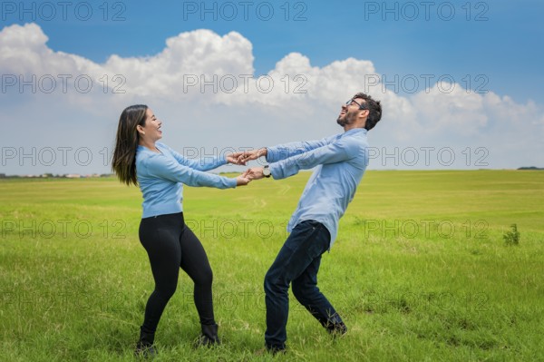 Happy couple spinning in a circle in the field, happy young couple spinning and playing in the field, young couple spinning in the field