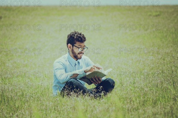 Young man on the grass reading a book, A person sitting on the grass reading a book, concept of people reading outside