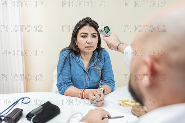 Doctor taking temperature to woman patient in office. Male doctor taking temperature with gun to patient. Doctor measuring temperature with infrared gun to female patient