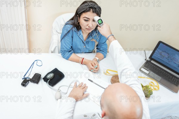 Male doctor taking temperature with gun to patient. Doctor measuring temperature with infrared gun to female patient, Doctor taking temperature to woman patient in office