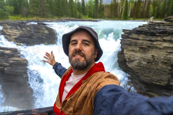 Happy tourist taking a selfie with powerful athabasca falls cascading into a narrow gorge in the background, showcasing the stunning natural beauty of jasper national park
