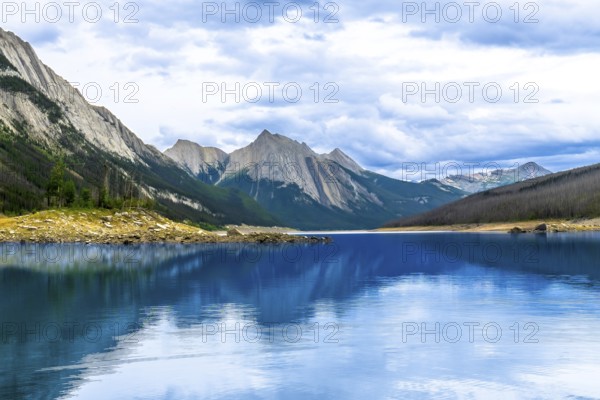 Calm turquoise water of medicine lake reflecting surrounding mountains under a cloudy sky in jasper national park, a unesco world heritage site, during a cloudy summer day