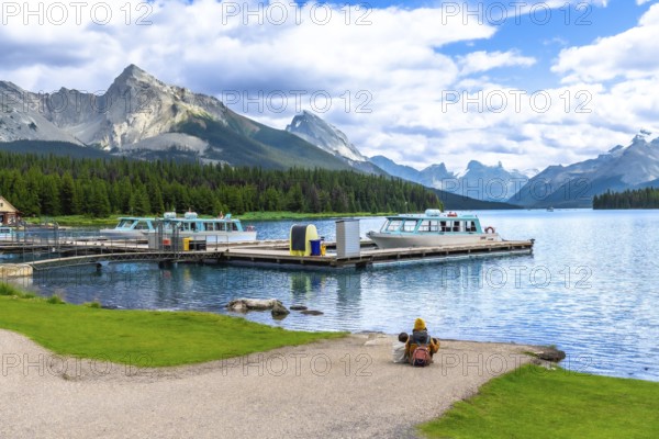 Tourists are enjoying the breathtaking view of maligne lake with tour boats and spirit island in the distance, surrounded by the majestic canadian rockies in jasper national park, alberta, canada