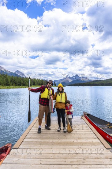 Family wearing life jackets standing on a wooden dock, ready for canoeing on maligne lake with the canadian rockies in the background, enjoying summer vacation in jasper national park