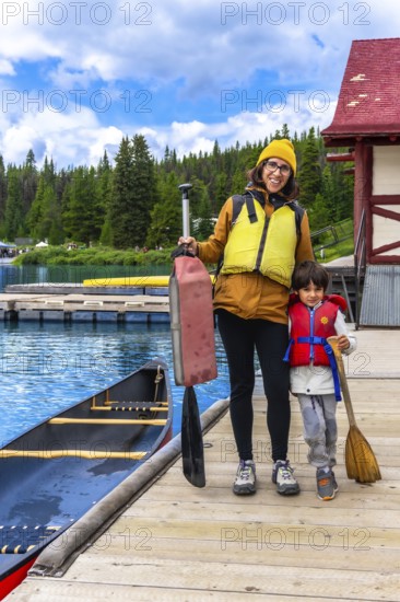 Mother and son holding paddles and wearing life jackets, getting ready for a canoe trip on the stunning maligne lake in jasper national park, alberta, canada