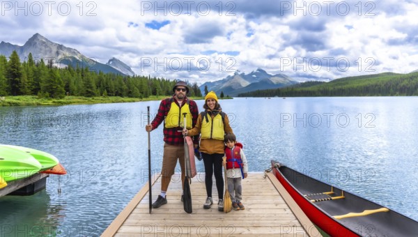 Family wearing life jackets and holding paddles, standing on a wooden dock with canoes and kayaks, enjoying a day of paddling on maligne lake in jasper national park