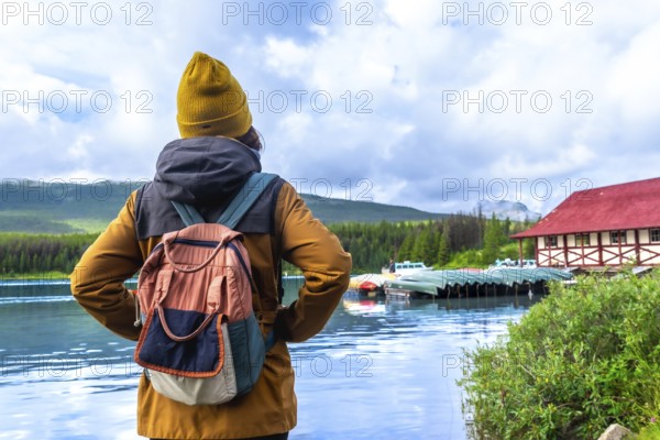 Female tourist with a backpack admiring the stunning view of maligne lake and its historic boathouse in the serene landscape of jasper national park, alberta