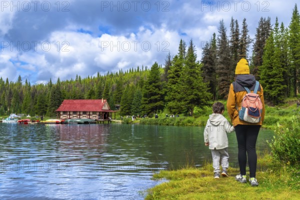 Mother and son admiring the beautiful landscape of maligne lake with its boathouse and colorful canoes in jasper national park, alberta, canada, during a sunny summer day