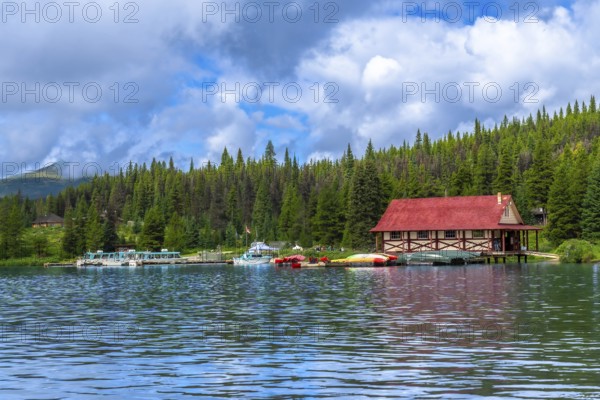 Colorful canoes and tour boats are docking at a boathouse with a red roof on maligne lake in jasper national park in the canadian rockies of alberta, canada, under a partly cloudy sky