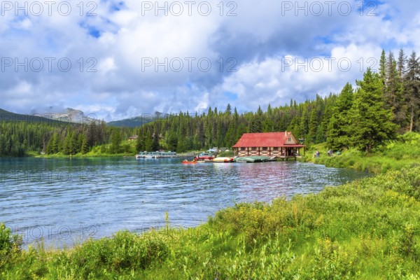 Beautiful summer landscape featuring a vibrant red roofed boathouse on the serene shores of maligne lake in jasper national park, alberta, with lush greenery and boats