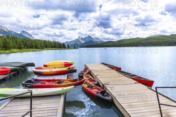 Colorful canoes and kayaks resting on a wooden dock invite exploration of maligne lake's pristine waters, surrounded by the majestic canadian rockies under a cloudy sky